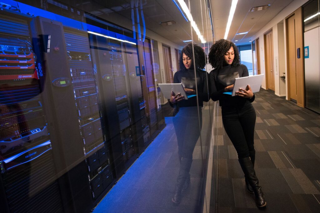 A person reviewing data on a tablet in a data center hallway lined with server racks, evoking AI agent infrastructure oversight